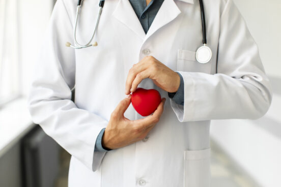 A doctor in a white coat with a stethoscope holds a red heart-shaped object in their hands, symbolizing heart health and medical care.