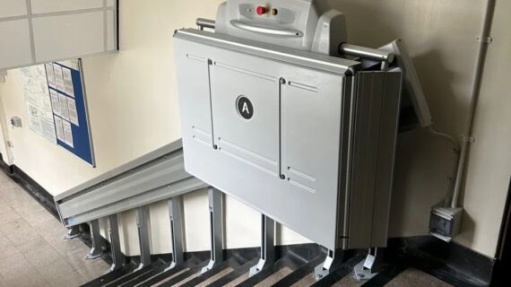 ACCESS BDD inclined platform lift (supra linea) folded in a compact and discrete design on an indoor staircase against a white wall.