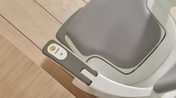 A close-up view of a gray HomeGlide Stair Lifts seat and control arm, positioned on a light wooden staircase, with a labeled button reading Alarm.