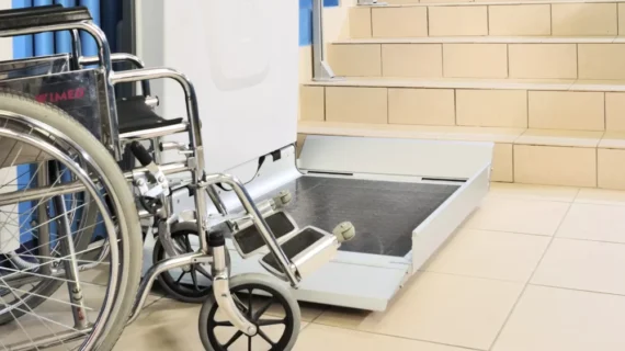 A wheelchair next to an open Supra Linea stairlift platform at the base of a staircase, showing accessible support for people with mobility impairments.