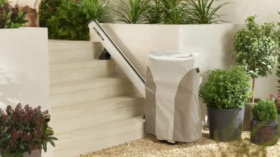 A HomeGlide Outdoor Stair Lift is installed beside outdoor steps surrounded by green potted plants and shrubs, seamlessly blending into the garden setting.