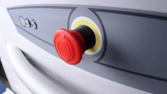 Close-up of a red emergency stop button on a gray HomeGlide Outdoor Stair Lift control panel, with a white handle visible below the button.