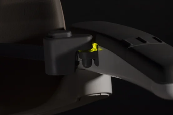 Close-up of a car seat armrest with a black and yellow latch mechanism, partially illuminated by Light Assist against a dark background.