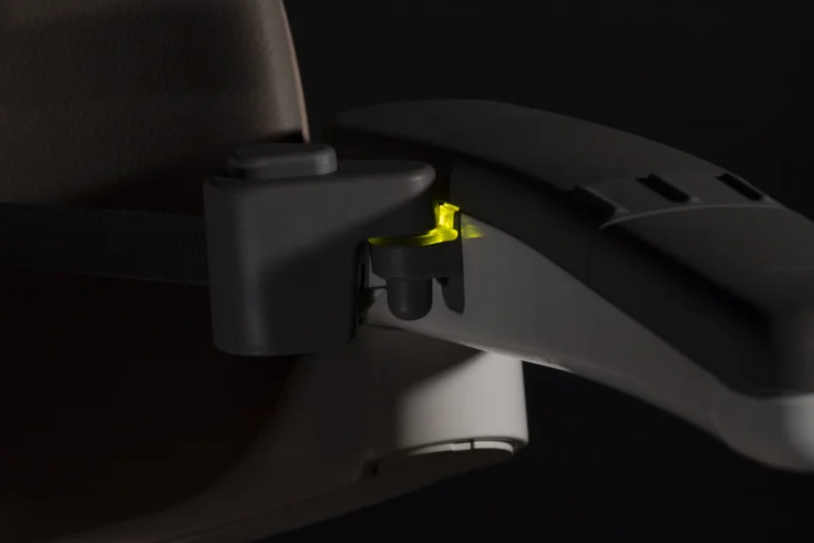 Close-up of a car seat armrest with a black and yellow latch mechanism, partially illuminated by Light Assist against a dark background.
