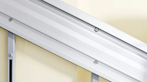 Close-up view of a silver metal HomeGlide Outdoor Stair Lift rail installed along a cream-colored wall, highlighting the smooth surface and mechanical details of the rail system.
