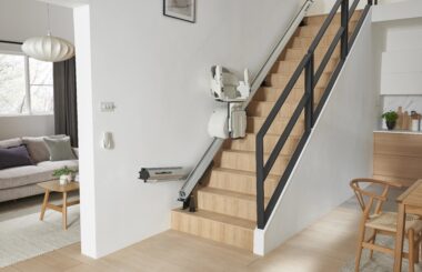 Straight stair lift with a hinged rail installed on a residential staircase, allowing the lower section of the track to fold upward and keep the hallway clear when the lift is not in use.
