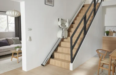 Straight stair lift installed along a wooden staircase in a modern home, featuring a foldable seat, armrests, and footrest parked midway on the rail system to provide safe and convenient access between floors.