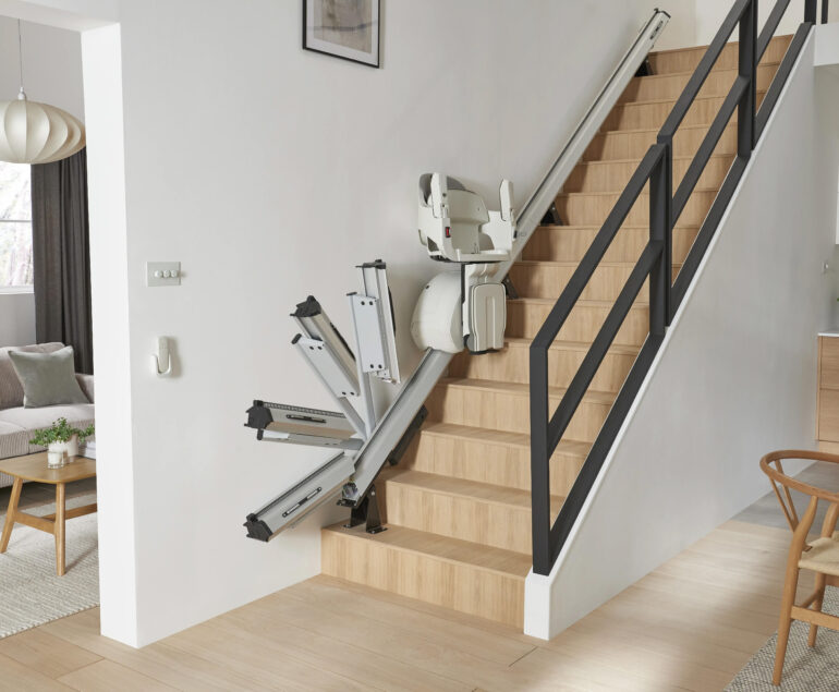 HomeGlide Stairlift by ACCESS BDD demonstrating the folding rail feature in motion in a residential home on a wooden staircase to improve independence.