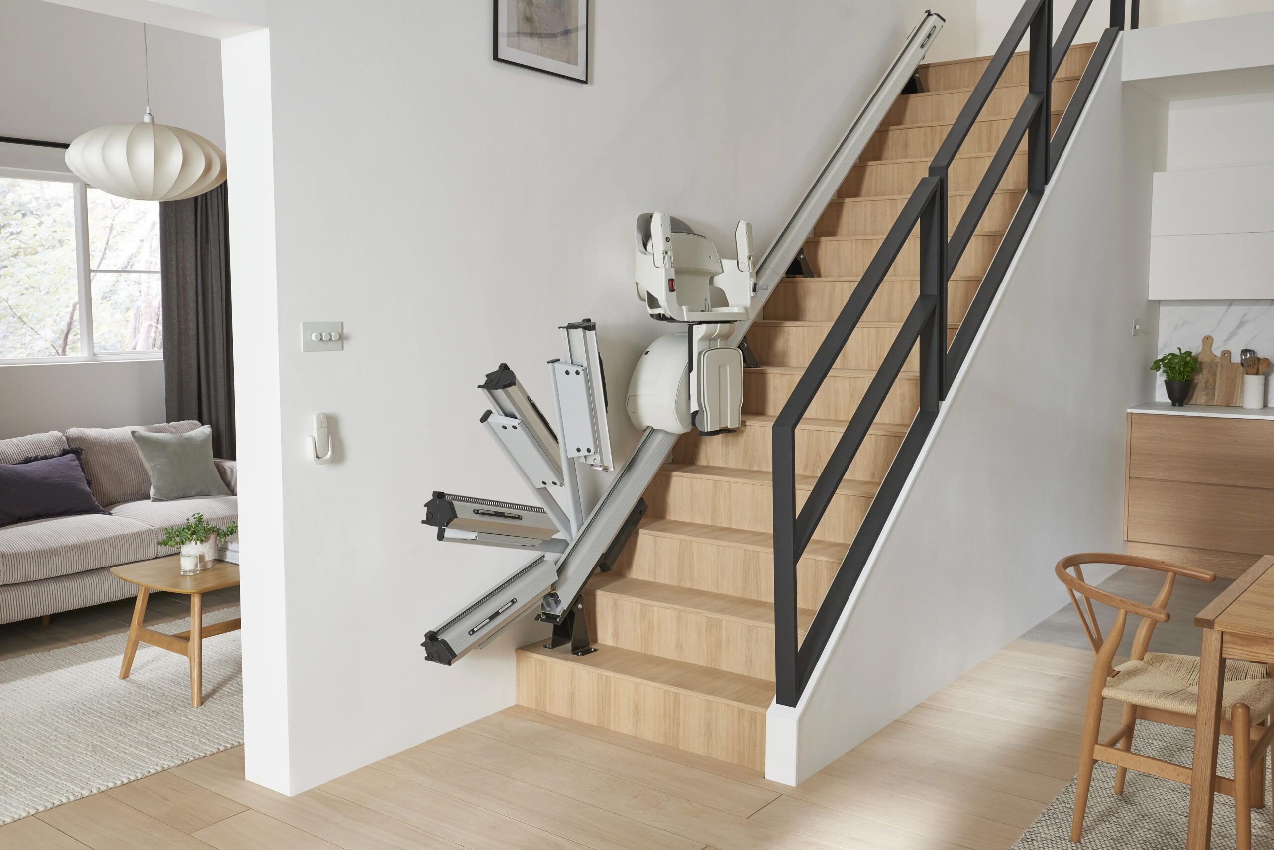 HomeGlide Stairlift by ACCESS BDD demonstrating the folding rail feature in motion in a residential home on a wooden staircase to improve independence.