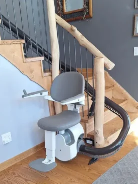 Flow X stair lift by ACCESS BDD completed installation on a wooden curved staircase with black rails and grey seating.