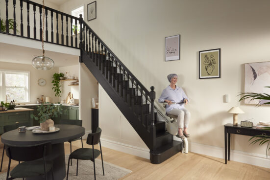 Older woman using a flow x stairlift on a straight staircase inside a home.
